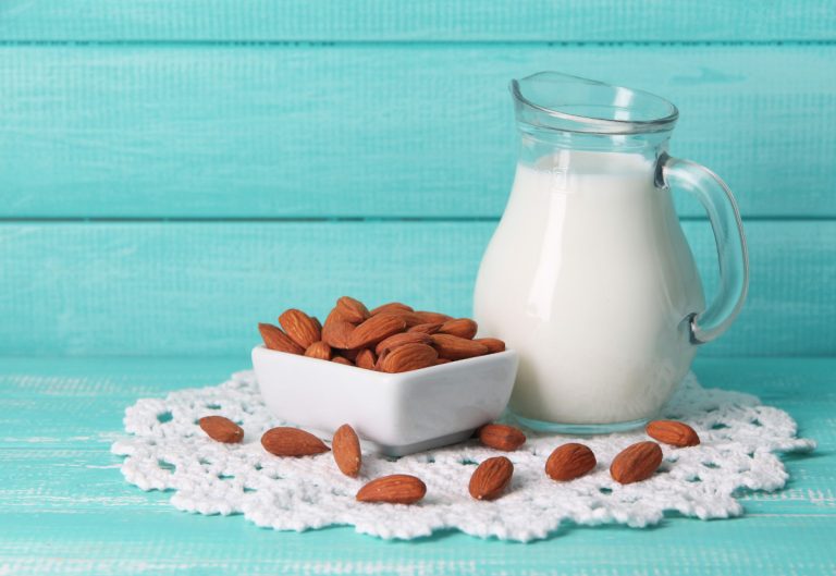 Almond milk in jug with almonds in bowl