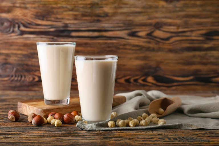Glasses of hazelnut milk on dark wooden background