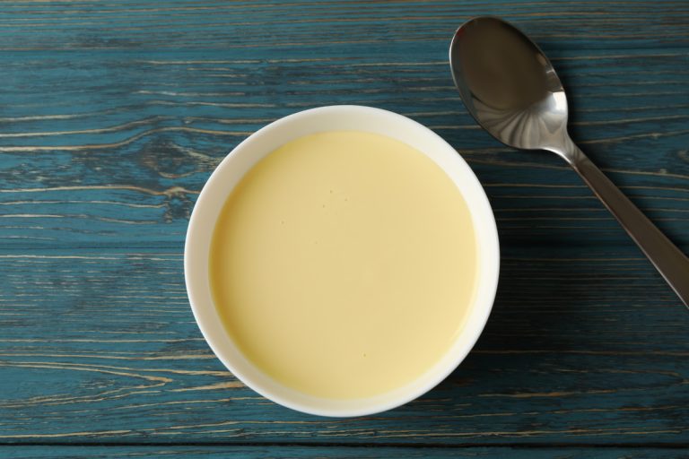 Spoon and bowl with condensed milk on wooden background