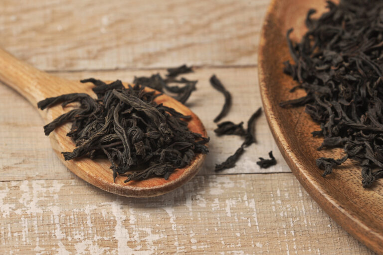 Black leaf tea on wooden spoon and wooden background