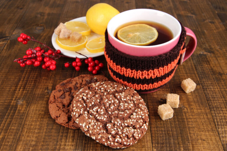 cup of tea with tea cozy, lemon, cookie, and sugar